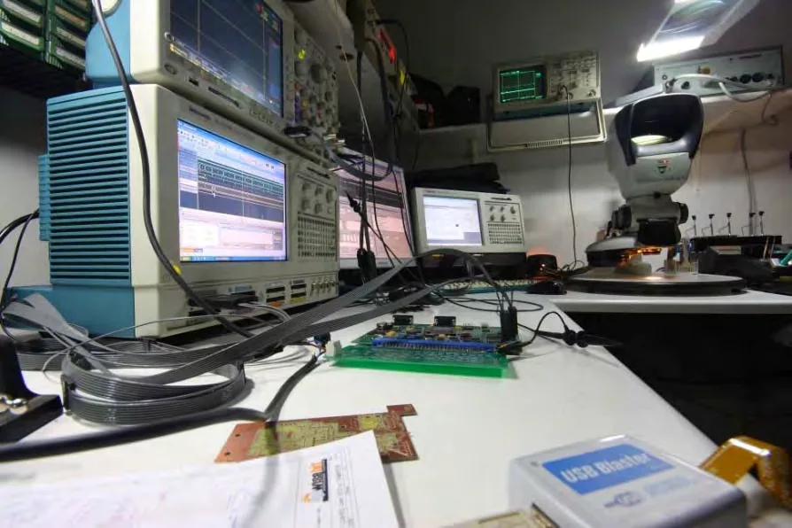 La Singularity Board in fase di sviluppo sul banco di laboratorio, tra strumenti di misura e monitor